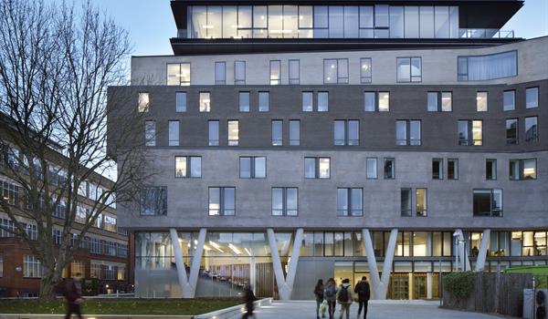 Queen Mary Graduate Centre, an eight storey building with glazing and angled columns at grade, brick facade that alternates from light to dark to light grey, and a glazed penthouse section on top